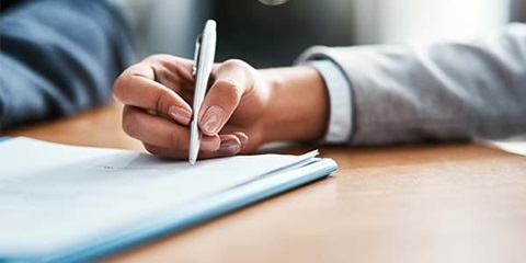 Hand mit Stift und Blatt Papier auf einem Tisch