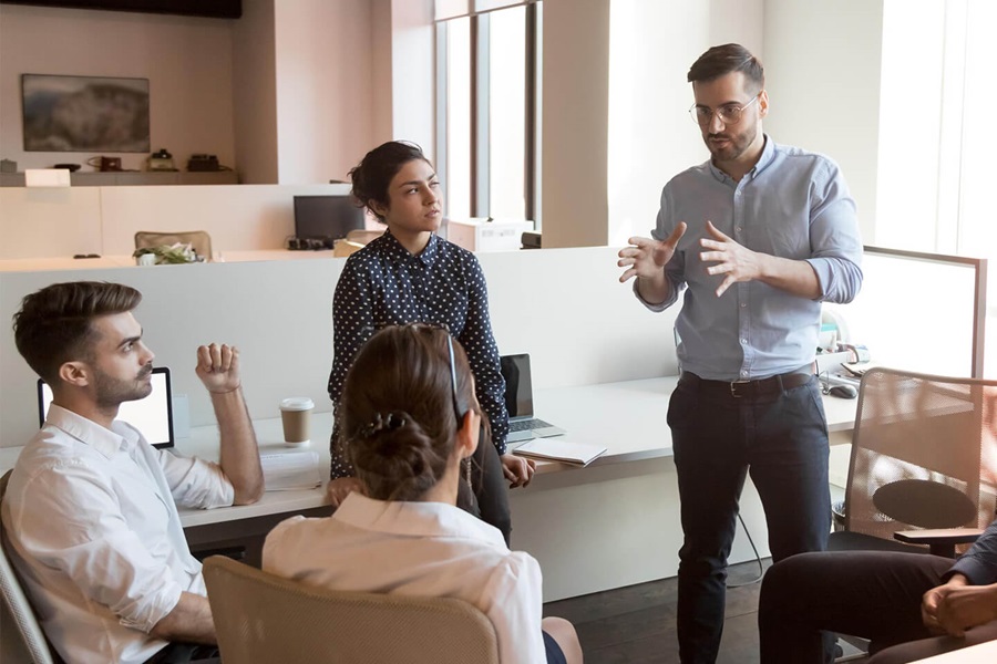 Teambesprechung im modernen Büro, stehender Mann gestikuliert während er drei sitzenden Kollegen erklärt